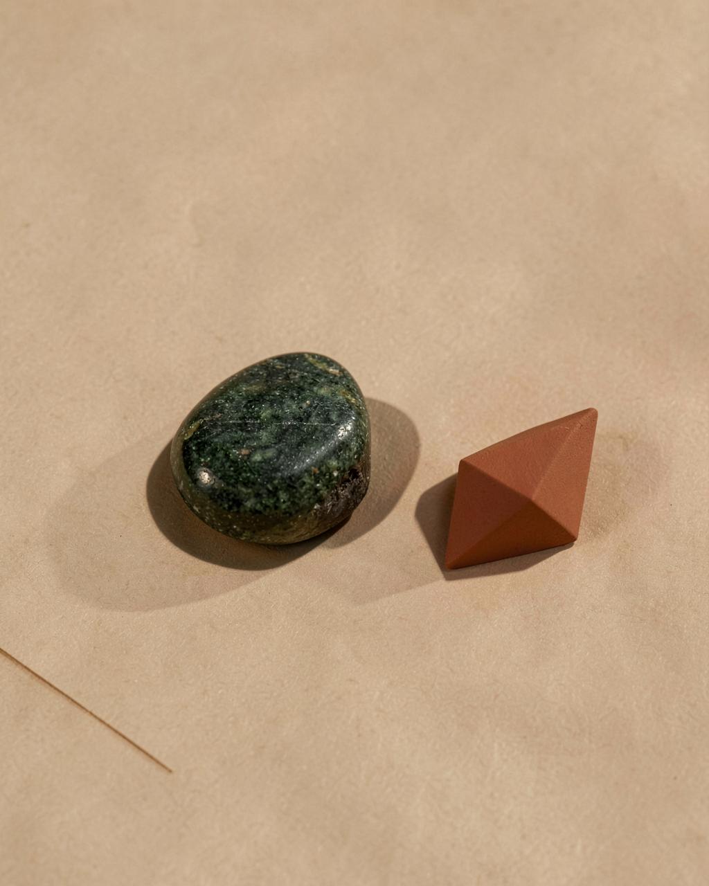 Polished stone and a matte geometric object on warm beige paper — a quiet study in balance